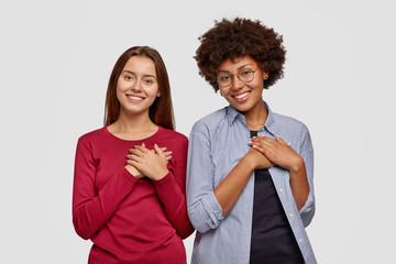 Wall Mural - Kind couple keep both hands on chest, express gratitude, being thankful for help, express good emotions and feelings, have pleasant smiles, isolated over white background. Gratitude concept.