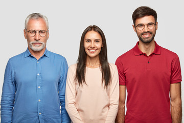 Wall Mural - Three people in shot. Serious senior male pensioner dressed in formal shirt, stands near his daughter and son, pose together against white backgrounf for making family portrait. Relationships concept