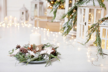 christmas candles and snowy fir branches over white wooden background with lights. new year's decora