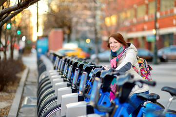 Happy young woman tourist ready to ride a rental bicycle in New York City at sunny spring day. Female traveler enjoying her time in downtown Manhattan.