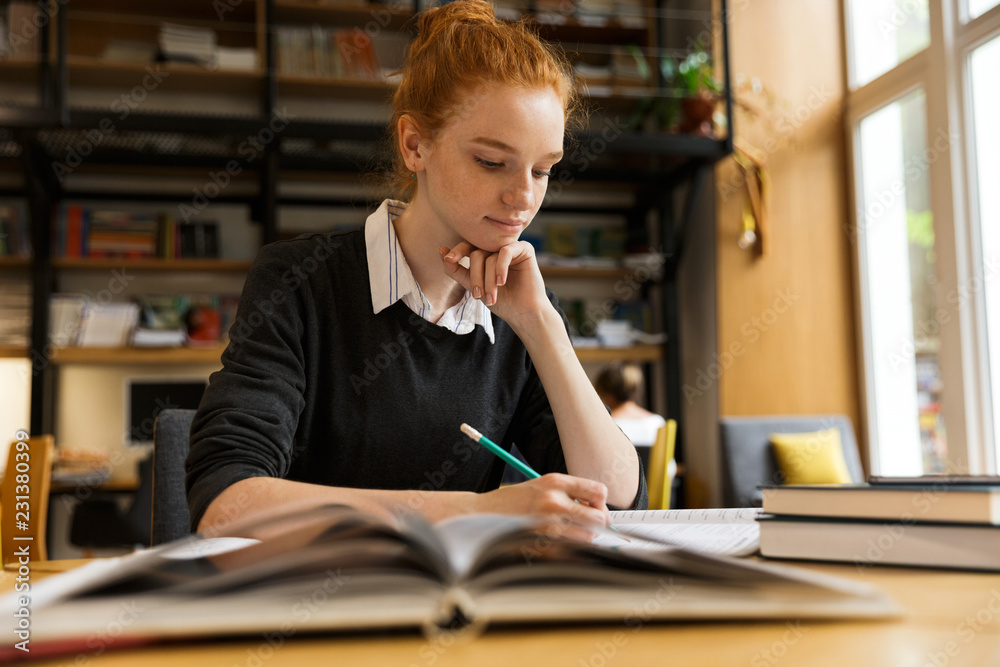 Lovely red haired teenage girl studying at the table - obrazy, fototapety, plakaty 