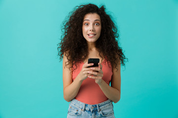 Wall Mural - Image of fashionable woman 20s wearing casual clothing holding black smartphone, standing isolated over blue background