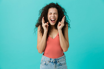 Poster - Image of beautiful woman 20s wearing casual clothing screaming and keeping fingers crossed, standing isolated over blue background