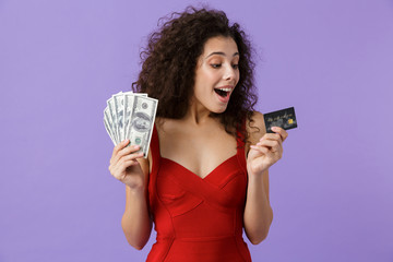 Wall Mural - Image of brunette woman 20s wearing red dress holding fan of money and credit card, standing isolated over violet background