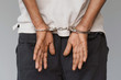 © polack - Close-up. Arrested man handcuffed hands at the back isolated on gray background. Prisoner or arrested terrorist, close-up of hands in handcuffs.