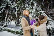 © Elizaveta - Young Caucasian boy with a beard and a girl have a date outdoors in the winter park against the background of a snowy conifer tree play snowballs, throw snow, hang themselves and play winter games