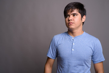 Wall Mural - Young Asian teenage boy wearing blue shirt against gray backgrou