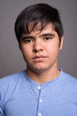 Wall Mural - Young Asian teenage boy wearing blue shirt against gray backgrou