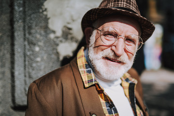 Close up portrait of hipster senior male with hat staying on urban street and looking straight at camera