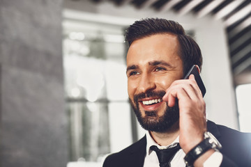 Beautiful smile. Positive young handsome man with dark hair and beard smiling and looking happy while talking on the phone