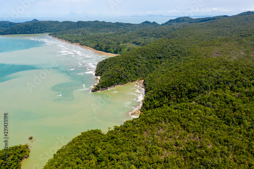 Fotomural Aerial drone view of dense tropical rainforest leading to a remote, rough ocean