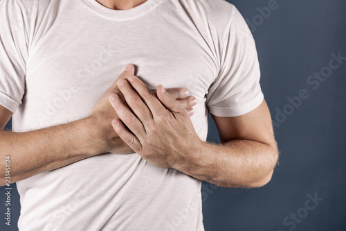 Fotografía Man holding his chest with both hands, having heart attack or painful cramps, pressing on chest with painful expression on blue backgound