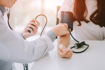 Doctor using sphygmomanometer with stethoscope checking blood pressure to a patient in the hospital.