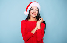 Beautiful Happy Young Cheerful Woman In Red And Santa Hat Posing On Pastel Blue Background