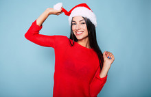 Beautiful Happy Young Cheerful Woman In Red And Santa Hat Posing On Pastel Blue Background