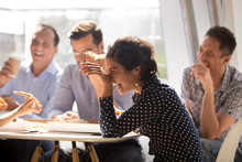 Indian Woman Laughing At Funny Joke Eating Pizza With Diverse Coworkers In Office, Friendly Work Team Enjoying Positive Emotions And Lunch Together, Happy Colleagues Staff Group Having Fun At Break