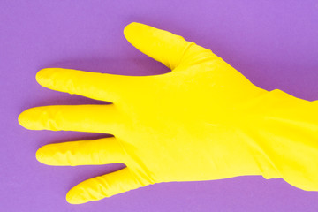 A hand in a yellow latex glove on a purple background demonstrates two spread fingers. Hand in a yellow rubber glove with fingers splayed on a pink background. For advertising cleaning.