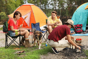 young people having lunch with sausages near camping tents outdoors