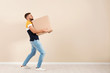 Full length portrait of young man carrying carton box near color wall. Posture concept