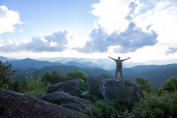 Mountaineer celebrating reaching the summit of a high rocky peak standing with his arms raised looking out over a vista of mountain ranges