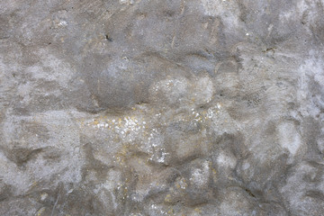 Details of grey rendered lumpy stone wall with small cracks and white flecks