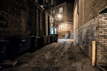 Dark And Scary Downtown Urban City Street Corner Alley With An Eerie Vintage Industrial Warehouse Factory Entrance And Dirty Dumpsters At Night