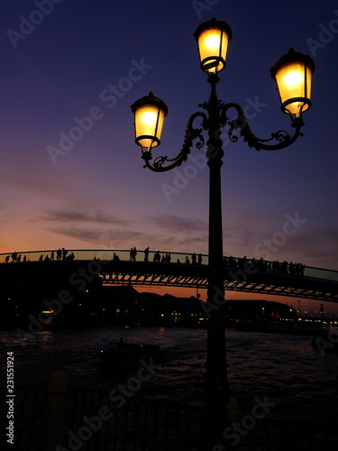 Fotografía An old street lantern and silhouettes of people on the bridge crossing The Grand Canal