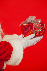 Photo of Santa Claus gloved hand with giftbox, on a red backgrou