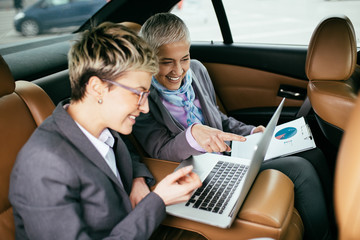 Wall Mural - Senior business woman and her assistant sitting in limousine talking and working.