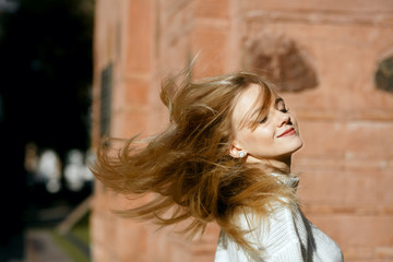 Closeup portrait of young model with fluttering hair posing near wall. Space for text