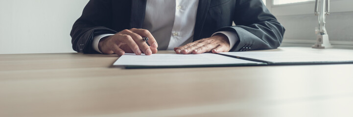 Wall Mural - Wide view image of businessman sitting at his office desk with pen in one hand