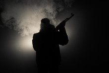 Silhouette Of Man With Assault Rifle Ready To Attack On Dark Toned Foggy Background Or Dangerous Bandit In Black Wearing Balaclava And Holding Gun In Hand. Shooting Terrorist With Weapon Theme Decor