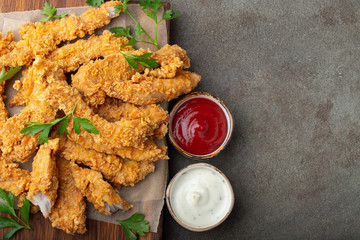 Breaded chicken strips with two kinds of sauces on a wooden Board. Fast food on dark brown background. Top view with copy space