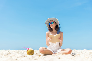 Summer Vacation. Smelling asian women relaxing and reading book on the beach, so happy and luxury in holiday summer, blue sky background. Travel and lifestyle Concept.