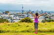 Auckland city skyline view from Mount Eden of Sky tower, New Zealand. Happy woman with arms up in freedom and happiness at top of Mt Eden urban park famous tourist attraction.