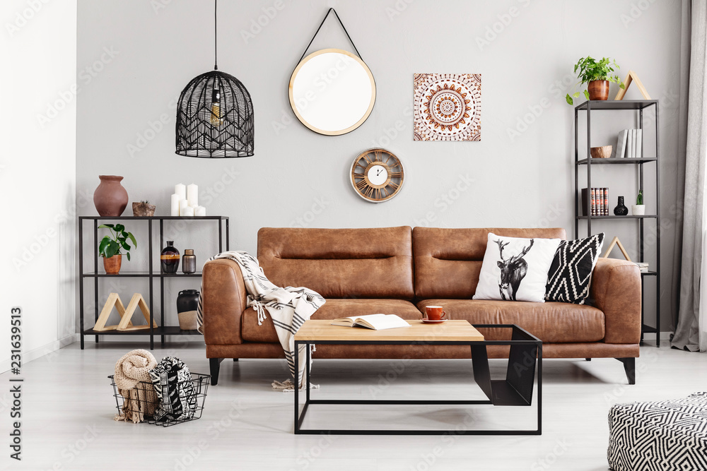 Leather sofa with pillows and blanket in the middle of elegant living room interior with metal shelves and modern coffee table, real photo - obrazy, fototapety, plakaty 