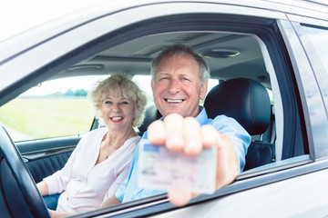 portrait of a happy senior man showing his available driving license while sitting in the car next t