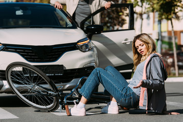 partial view of young female bicycle rider mowed down by driver in car on road, car accident concept