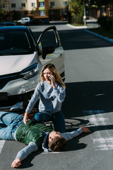 Wall Mural - high angle view of young woman calling emergency white injured cyclist lying on road after car accident