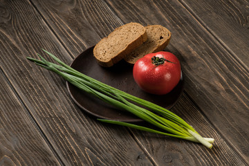 Tomato, green onion and pieces of bread on a wooden background