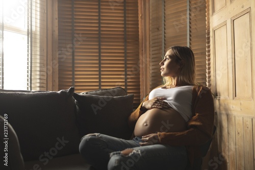 женщина держится за живот и задумчиво смотрит в окно