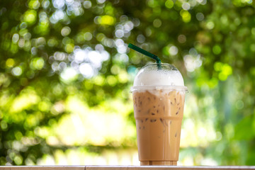 Ice cappuccino in plastice cup. Take away package. Beverage with green nature bokeh background.