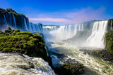 Water cascading over the Iguacu falls with rainbow in foreground in Brazil