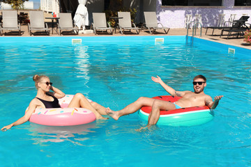 Poster - Happy young couple with inflatable rings in swimming pool