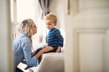 Wall Mural - A young mother talking to her toddler son inside in a bedroom.