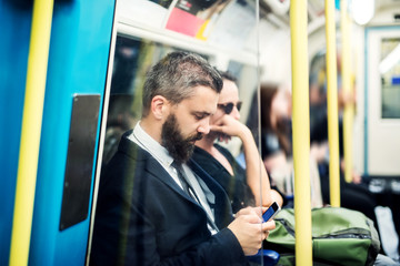 Wall Mural - Hipster businessman with smartphone inside the subway in the city, travelling to work.