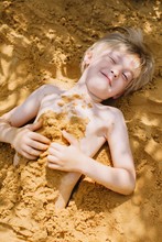 Adorable Happy Blond Toddler Laying On Sand And Covered With It
