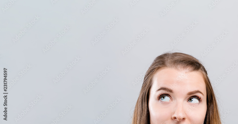 Young woman looking upwards on a gray background - obrazy, fototapety, plakaty 