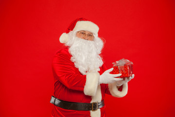 Photo of Santa Claus gloved hand with giftbox, on a red backgrou