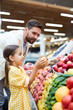 © pressmaster - Serious handsome bearded father teaching daughter to pick up fruits at farmers market
